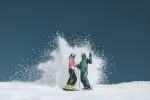 Two snowboarders creating a spray of snow on the slopes
