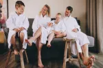 Familie in weißen Bademänteln sitzt auf einem Sofa, entspannt und lacht.