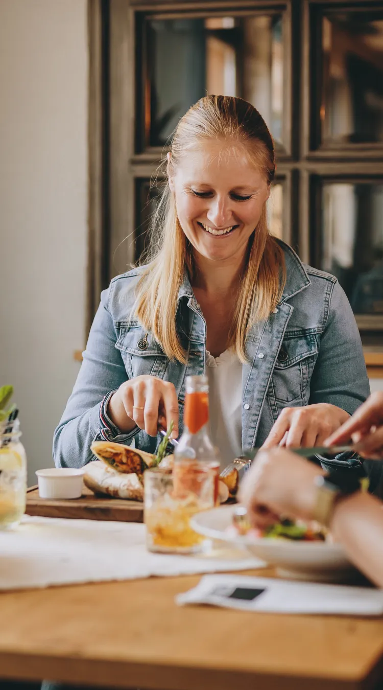 Lachende Frau am Tisch mit Essen und Getränken, gemütliches Ambiente