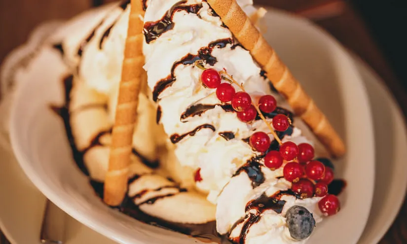 Dessert mit Eis, Schokolade, roten Johannisbeeren und Waffelröllchen
