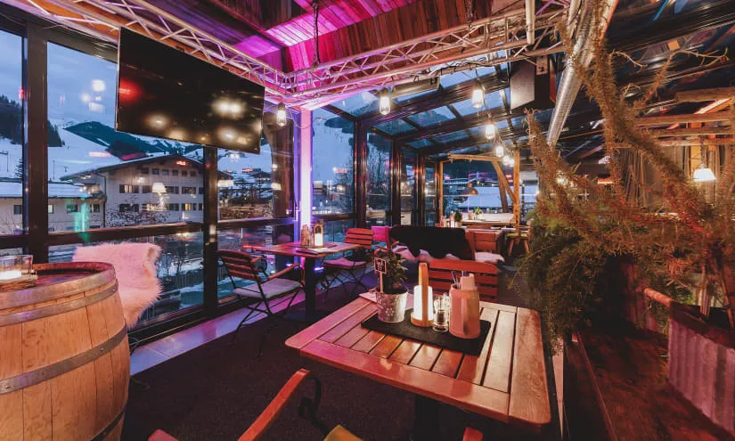 Gemütliches Interieur mit Bar, Holzdekor und großem Bildschirm mit Blick auf eine verschneite Landschaft.