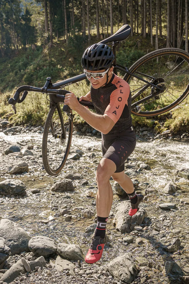 Radfahrer trägt sein Gravel-Bike über einen Bach in Saalbach-Hinterglemm