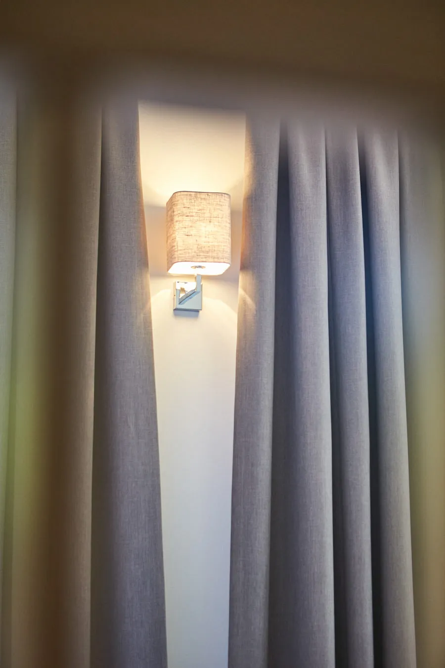 Wandleuchte zwischen grauen Vorhängen, unscharf im Hintergrund