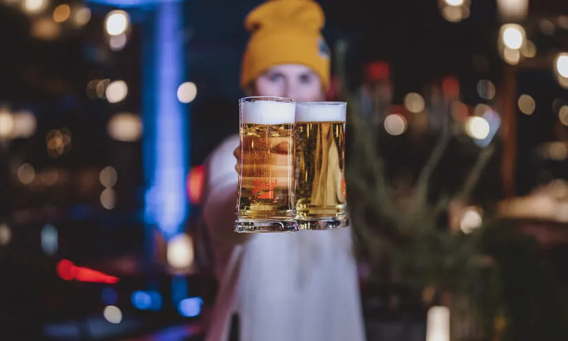 Person holding two glasses of beer in a bar setting