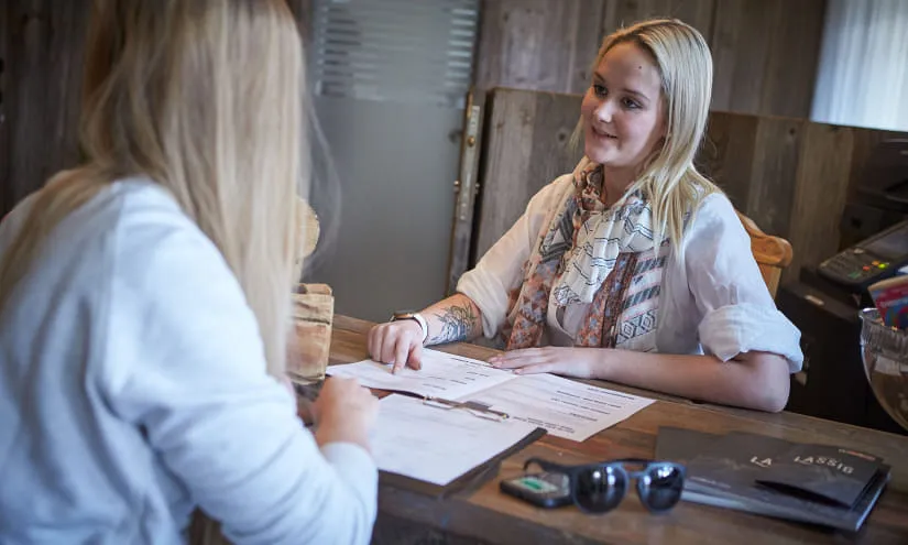 Two women at a reception desk, discussing paperwork in a cozy environment.