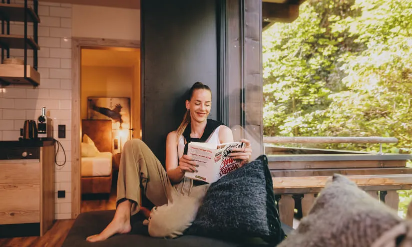 Frau liest eine Zeitschrift in einer modernen Wohnung mit Blick auf Bäume