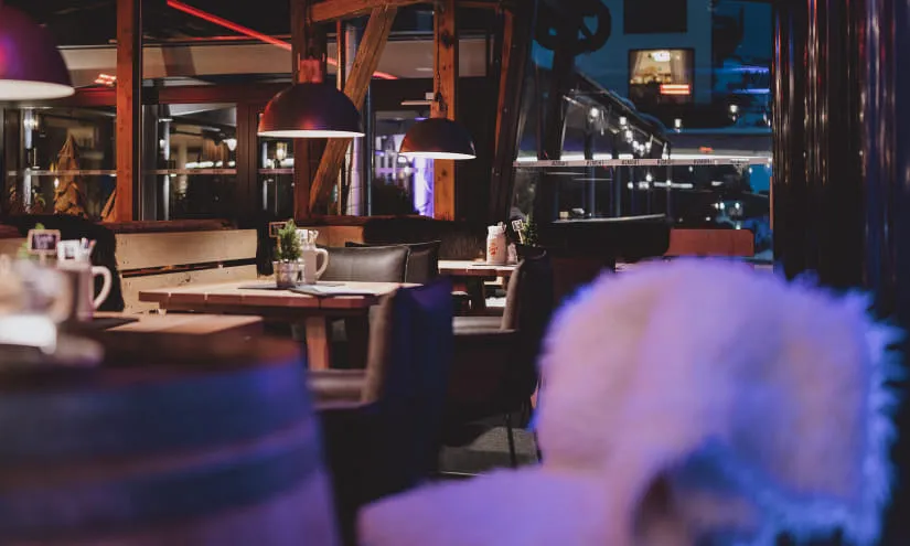 Innenansicht eines Restaurants mit Tischen und Stühlen, gedämpftem Licht.