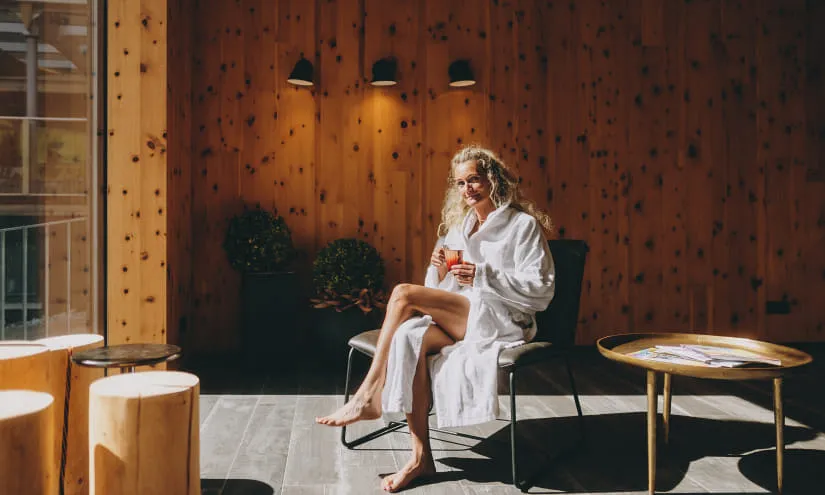 Frau in einem Bademantel sitzt auf einem Stuhl in einem Holzinterieur