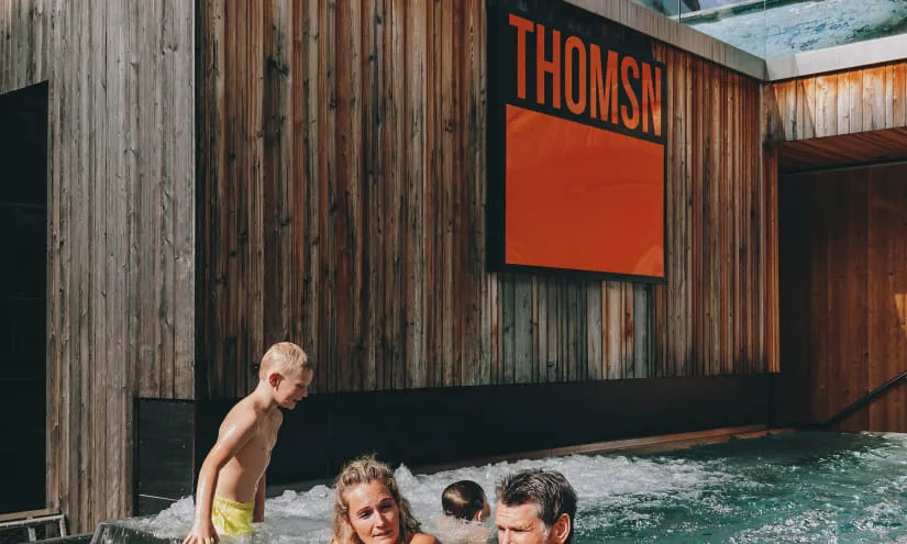 Familie entspannt im Whirlpool, Holzfassade mit THOMSN-Schild