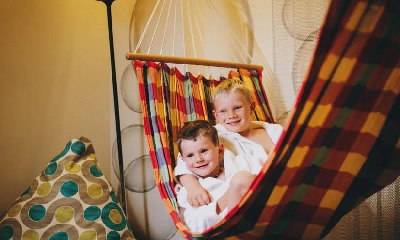 Zwei Kinder in einer bunten Hängematte mit einem runden gepunkteten Sitzsack in der Nähe