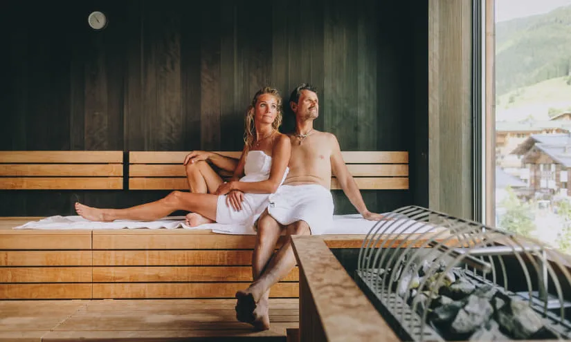 Paar in einem Wellnessbereich, entspannt auf einer Holzbank in einer Sauna.
