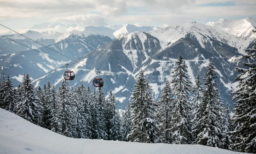 Seilbahn zwischen schneebedeckten Bergen und Tannen in Saalbach-Hinterglemm.