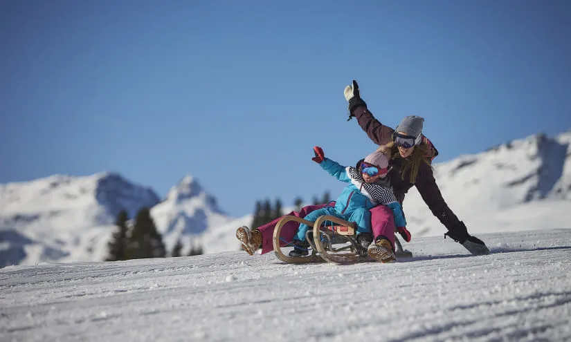 Frau und Kind rodeln auf Schnee in den Bergen