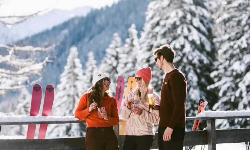 Zwei Personen stehen an einem Holzgeländer in den Bergen, umgeben von Skiern.