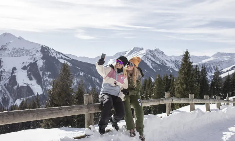 Zwei Frauen machen ein Selfie in einer verschneiten Berglandschaft im Winter
