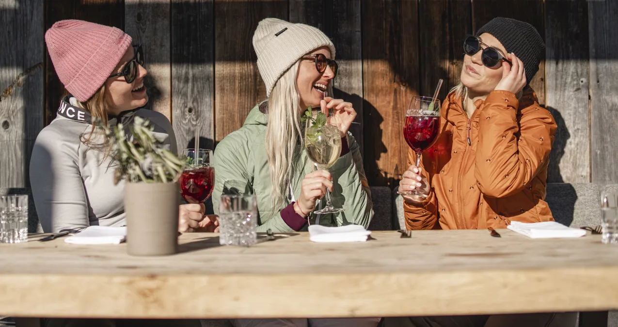 Drei Frauen genießen Getränke an einem Tisch im Freien.