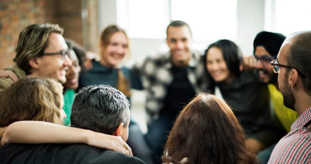 Gruppe von verschiedenen Menschen im Huddle, lächelnd und miteinander beschäftigt