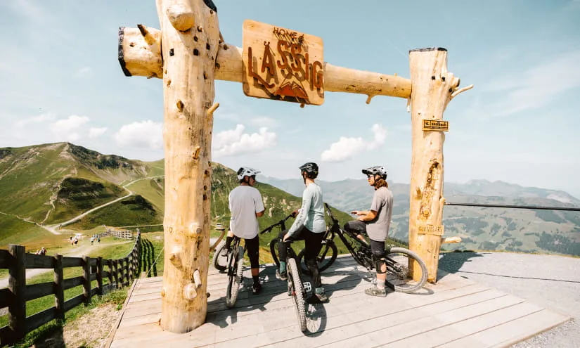 Drei Radfahrer stehen an einem hölzernen Tor mit Schild zur Bike-Route.