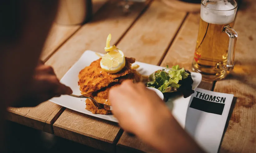 Teller mit einem Schnitzel und Salat auf Holztisch, Bier im Hintergrund