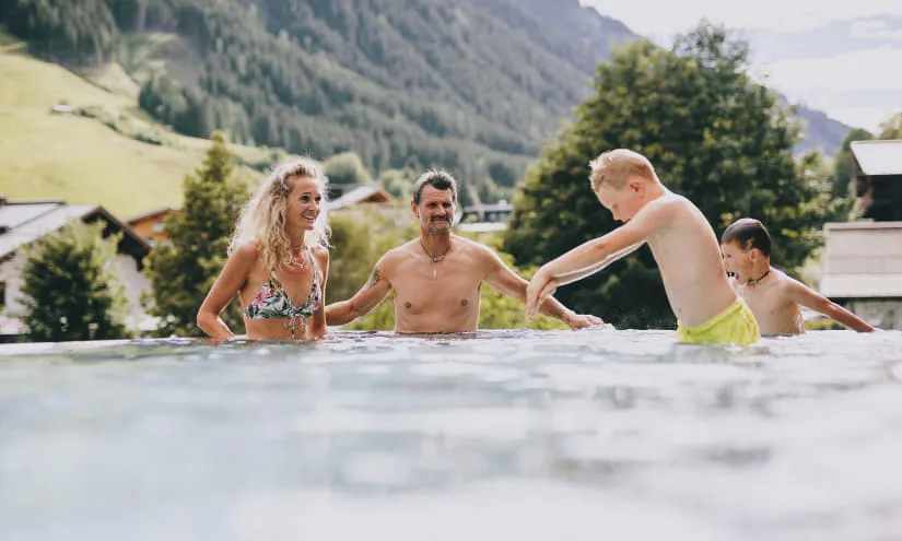 Familie im Wasser, umgeben von Bergen und Bäumen, im Freien.