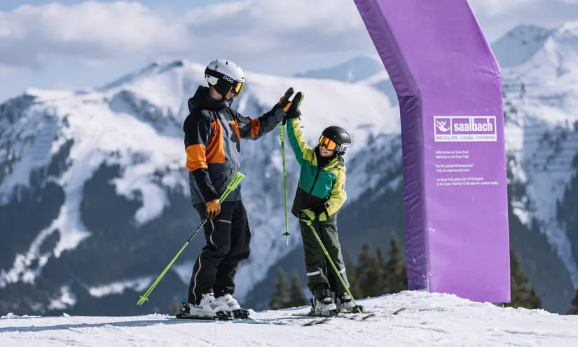 Vater hilft seinem Kind beim Skifahren in den Alpen von Saalbach.