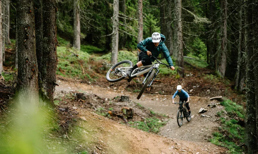 Mountainbiker springt über einen Hügel im Wald.