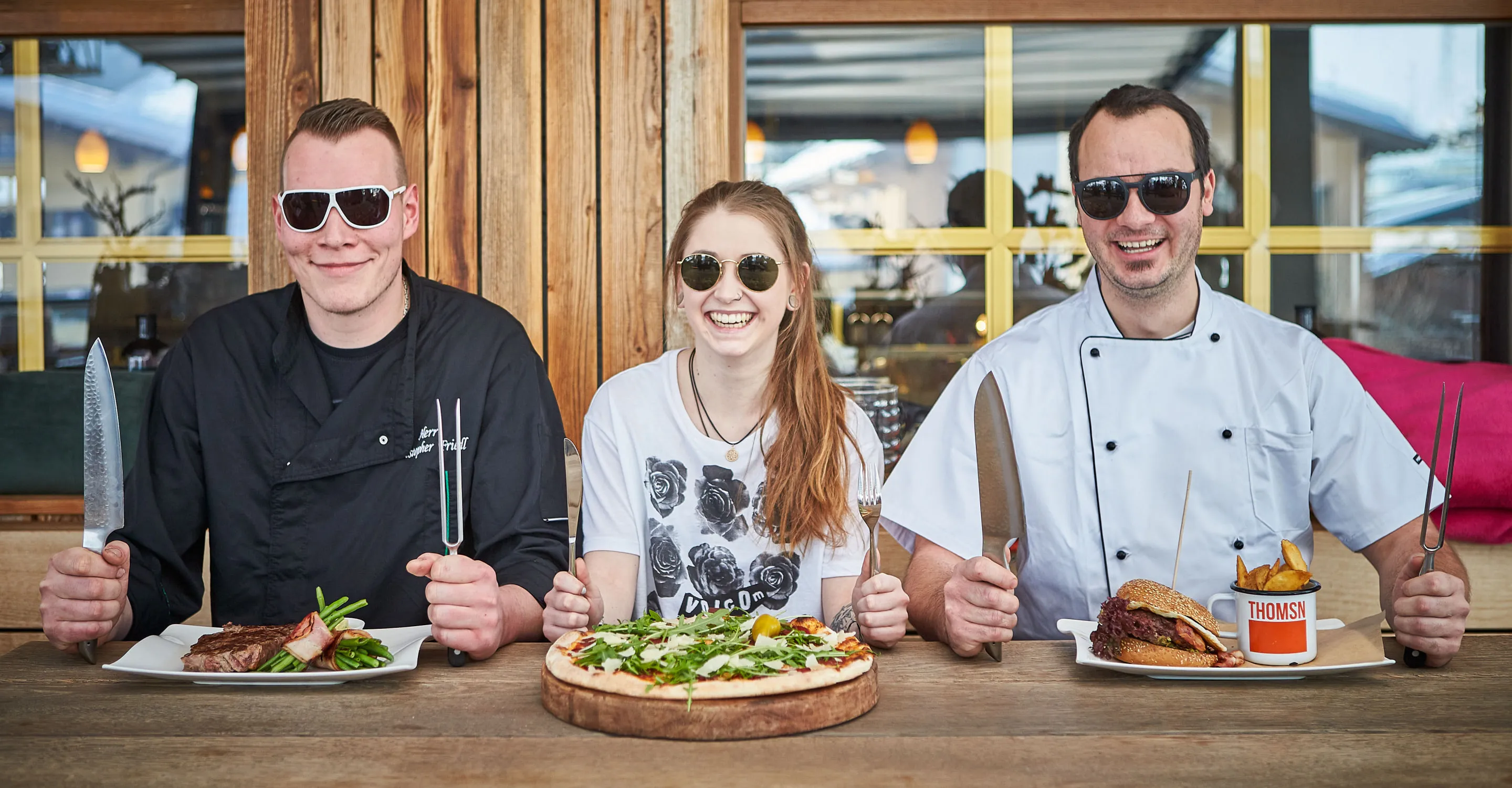 Three chefs with sunglasses and dishes in front of wood paneling
